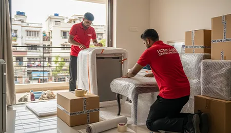 Professional movers carefully packing household items like furniture, appliances, and boxes in a residential apartment in India